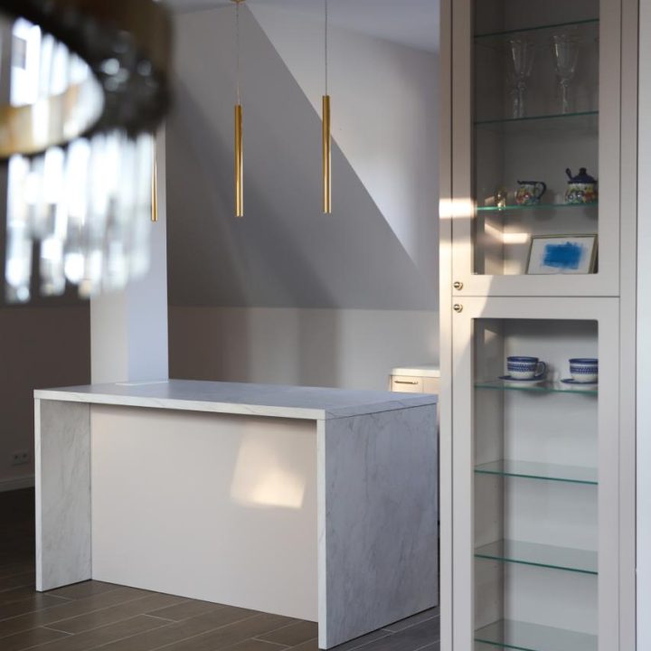 Kuchnia na wymiar w Warszawie – układ L, wyspa, witryna i szafa. Subtelna kolorystyka, marmurowe blaty i złote detale. Realizacja MiD Prestige w 8 tygodni.