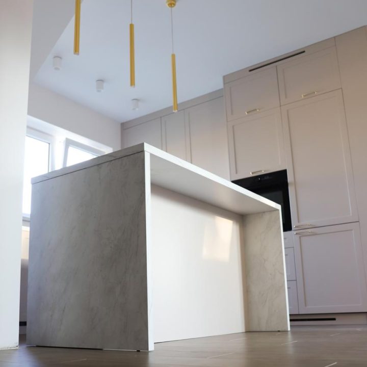 Kuchnia na wymiar w Warszawie – układ L, wyspa, witryna i szafa. Subtelna kolorystyka, marmurowe blaty i złote detale. Realizacja MiD Prestige w 8 tygodni.