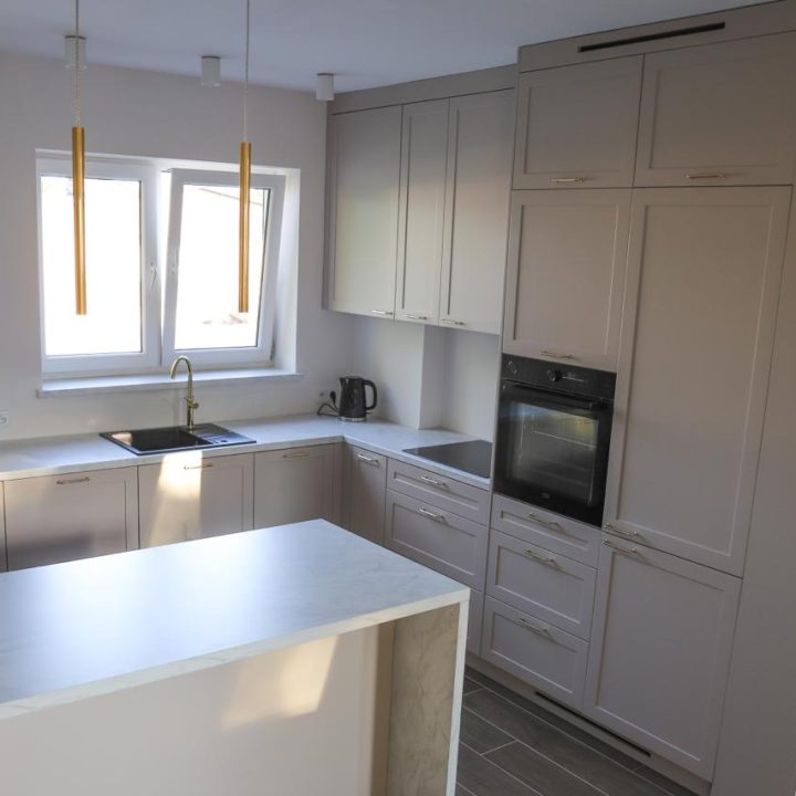 Kuchnia na wymiar w Warszawie – układ L, wyspa, witryna i szafa. Subtelna kolorystyka, marmurowe blaty i złote detale. Realizacja MiD Prestige w 8 tygodni.