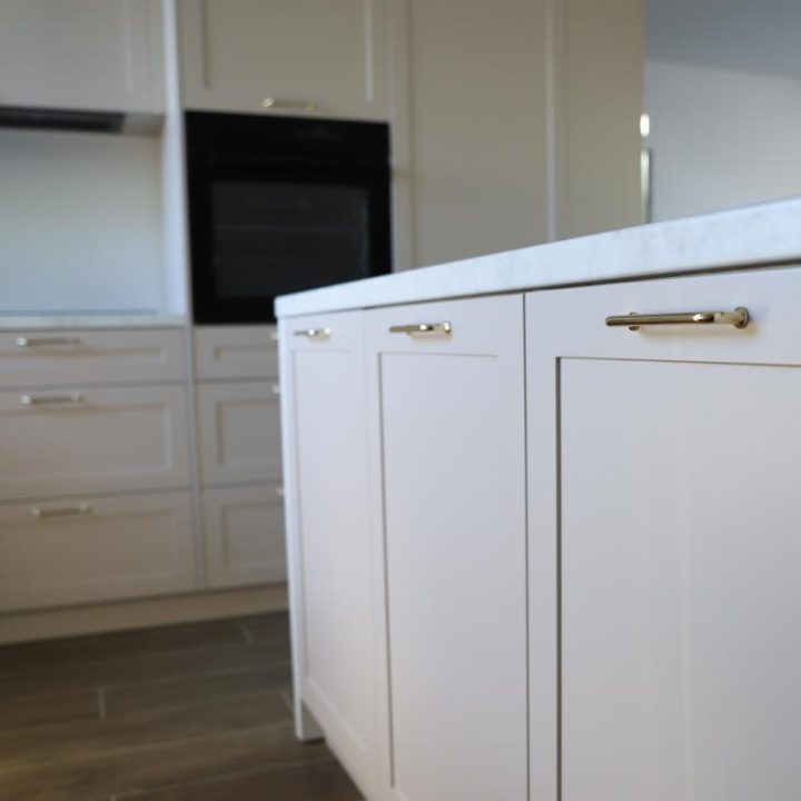 Kuchnia na wymiar w Warszawie – układ L, wyspa, witryna i szafa. Subtelna kolorystyka, marmurowe blaty i złote detale. Realizacja MiD Prestige w 8 tygodni.