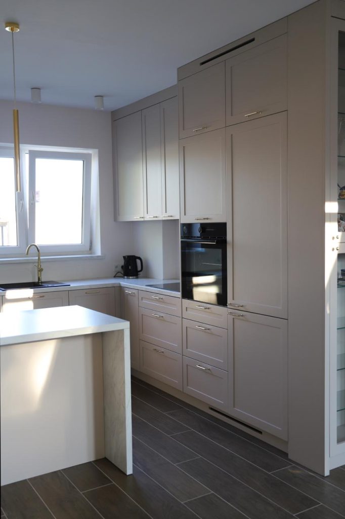 Kuchnia na wymiar w Warszawie – układ L, wyspa, witryna i szafa. Subtelna kolorystyka, marmurowe blaty i złote detale. Realizacja MiD Prestige w 8 tygodni.