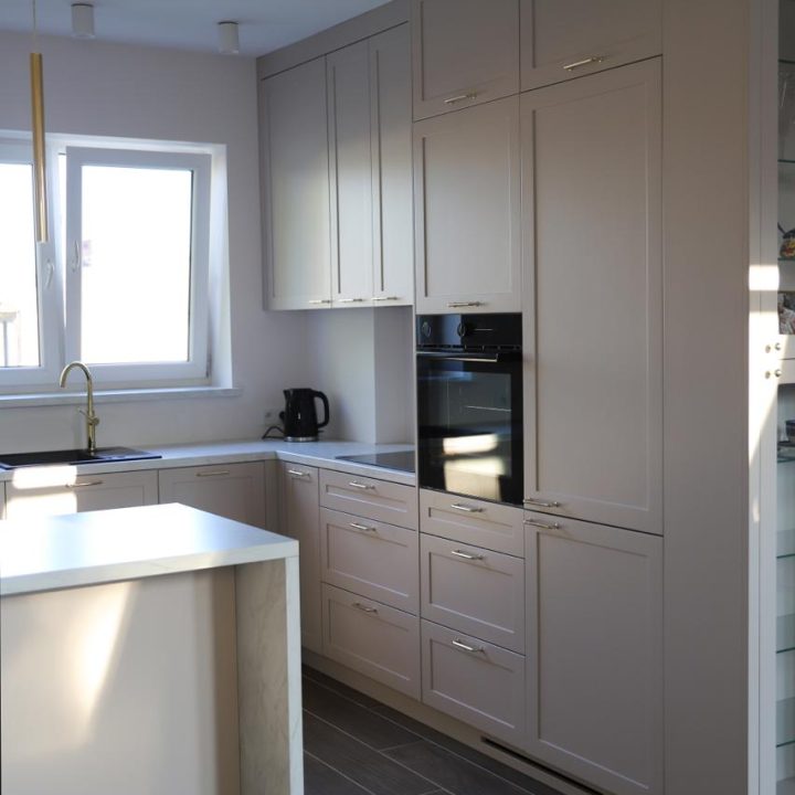 Kuchnia na wymiar w Warszawie – układ L, wyspa, witryna i szafa. Subtelna kolorystyka, marmurowe blaty i złote detale. Realizacja MiD Prestige w 8 tygodni.