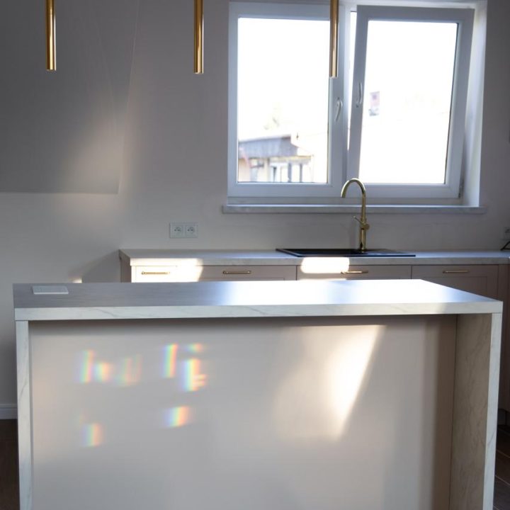 Kuchnia na wymiar w Warszawie – układ L, wyspa, witryna i szafa. Subtelna kolorystyka, marmurowe blaty i złote detale. Realizacja MiD Prestige w 8 tygodni.