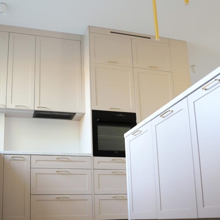 Kuchnia na wymiar w Warszawie – układ L, wyspa, witryna i szafa. Subtelna kolorystyka, marmurowe blaty i złote detale. Realizacja MiD Prestige w 8 tygodni.