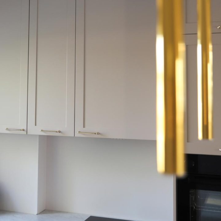 Kuchnia na wymiar w Warszawie – układ L, wyspa, witryna i szafa. Subtelna kolorystyka, marmurowe blaty i złote detale. Realizacja MiD Prestige w 8 tygodni.