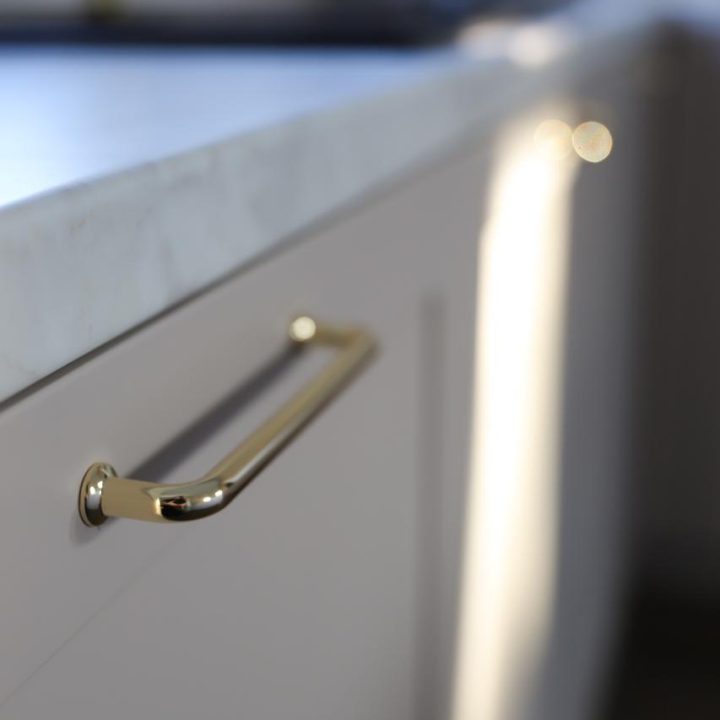 Kuchnia na wymiar w Warszawie – układ L, wyspa, witryna i szafa. Subtelna kolorystyka, marmurowe blaty i złote detale. Realizacja MiD Prestige w 8 tygodni.