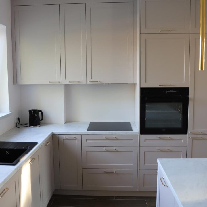 Kuchnia na wymiar w Warszawie – układ L, wyspa, witryna i szafa. Subtelna kolorystyka, marmurowe blaty i złote detale. Realizacja MiD Prestige w 8 tygodni.