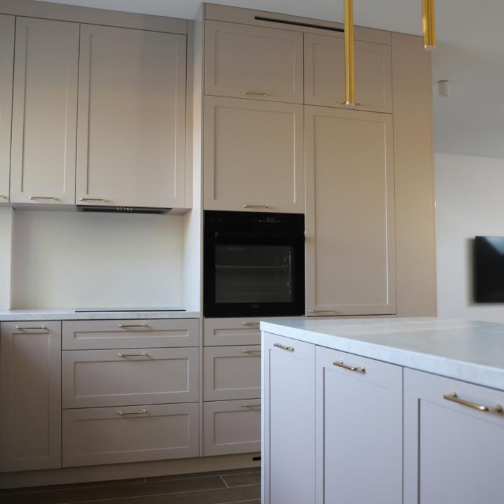 Kuchnia na wymiar w Warszawie – układ L, wyspa, witryna i szafa. Subtelna kolorystyka, marmurowe blaty i złote detale. Realizacja MiD Prestige w 8 tygodni.