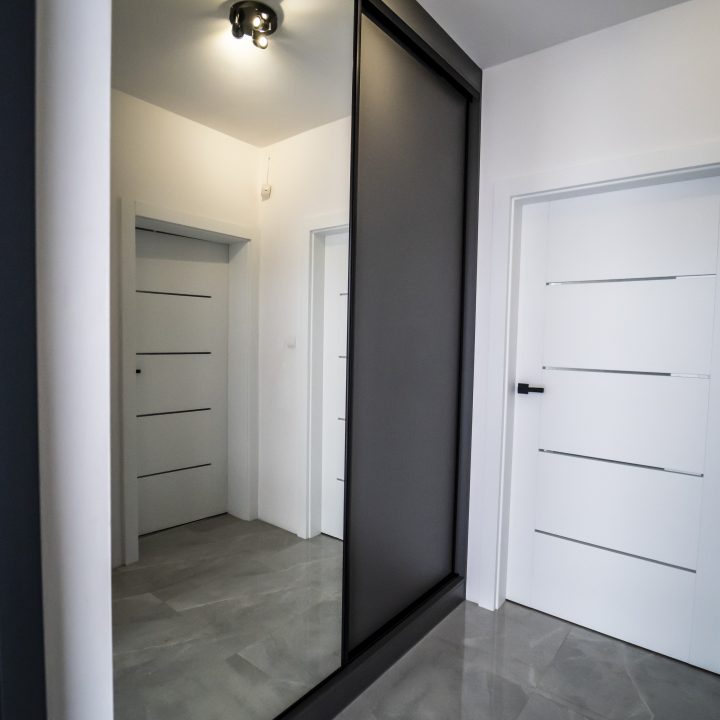 Nowoczesna kuchnia na wymiar w Pułtusku – biel i czerń w połysku, wyspa, oświetlenie LED i szafa we wiatrołapie. Styl, ergonomia i trwałość w pakiecie MiD Smart.